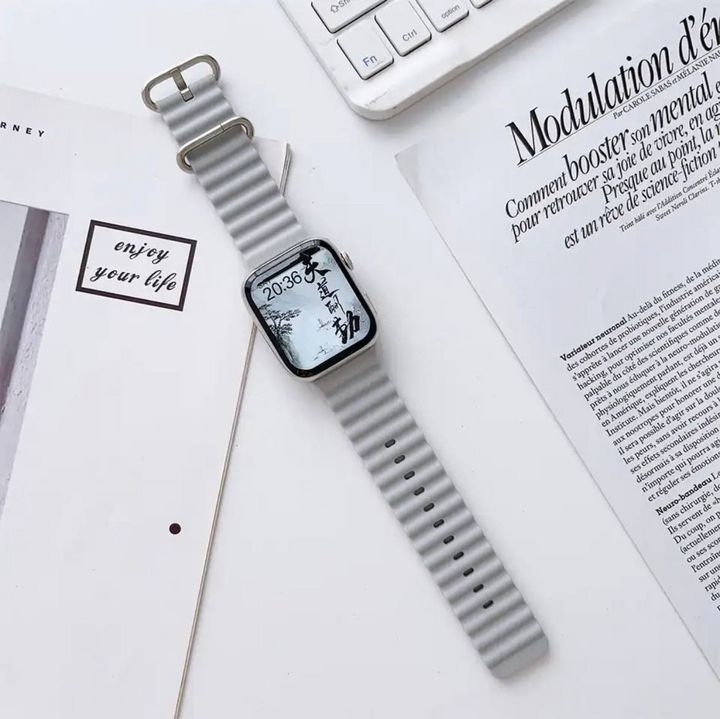  بند اپل واچ Slicto مدل Rubber Elastic Ocean Watch Straps به رنگ طوسی کنار یک صفحه کیبورد و چند برگه کاغذ 