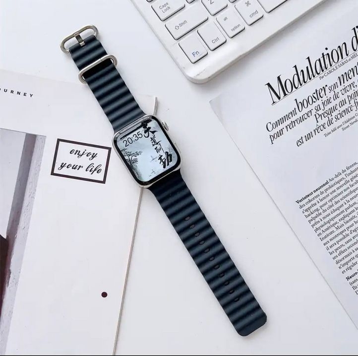  بند اپل واچ مدل Rubber Elastic Ocean به رنگ آبی سرمه‌ای که بر روی صفحه‌کلید و مجله‌ها قرار گرفته است. 