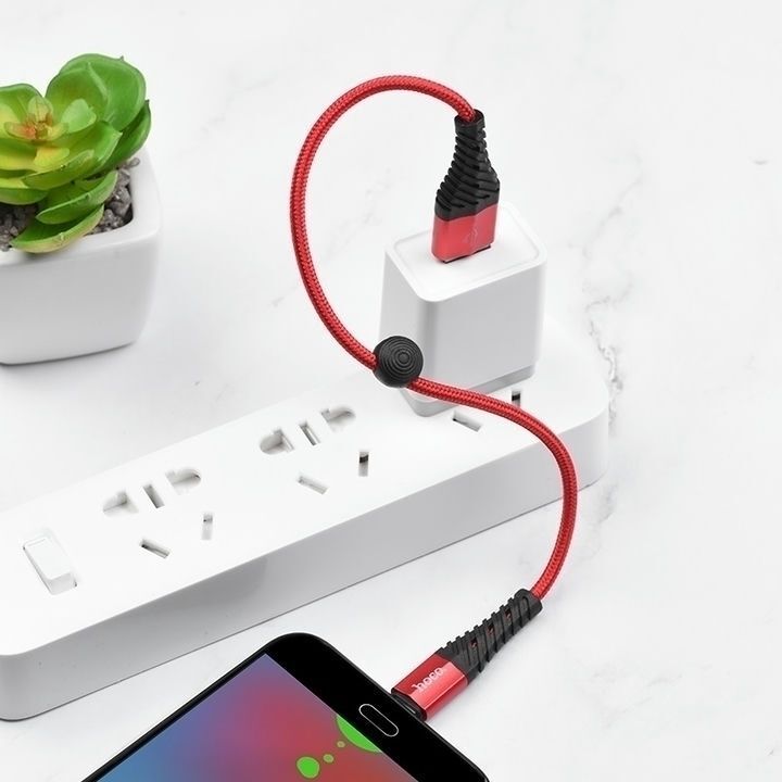  کابل قرمز رنگ USB به Micro USB هوکو مدل X38 به طول 0.25 متر، متصل به یک آداپتور شارژر و گوشی هوشمند روی یک پس‌زمینه سفید 